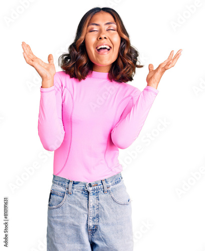 Young beautiful mixed race woman wearing pink shirt celebrating mad and crazy for success with arms raised and closed eyes screaming excited. winner concept