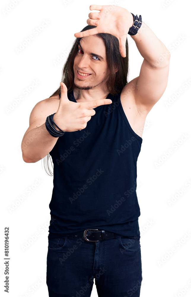 Young adult man with long hair wearing rocker style with black clothes and contact lenses smiling making frame with hands and fingers with happy face. creativity and photography concept. Young adult man with long hair wearing rocker style with black clothes and contact lenses smiling making frame with hands and fingers with happy face. creativity and photography concept.