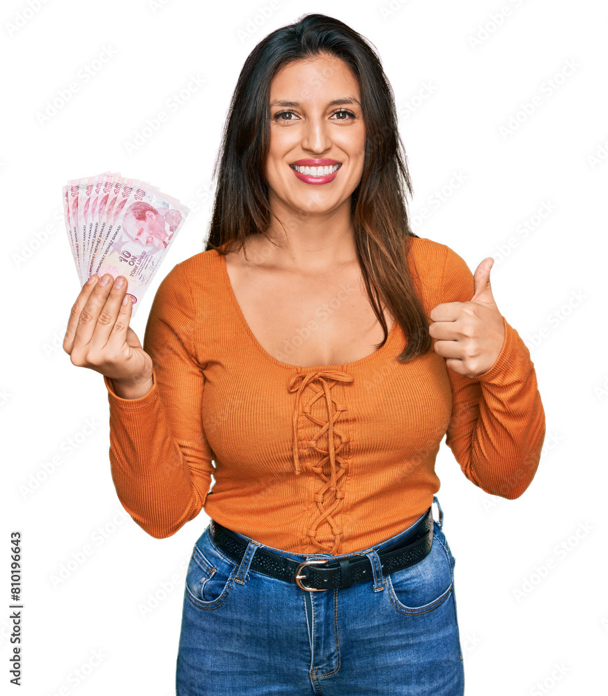 Beautiful hispanic woman holding 50 turkish lira banknotes smiling happy and positive, thumb up doing excellent and approval sign Beautiful hispanic woman holding 50 turkish lira banknotes smiling happy and positive, thumb up doing excellent and approval sign