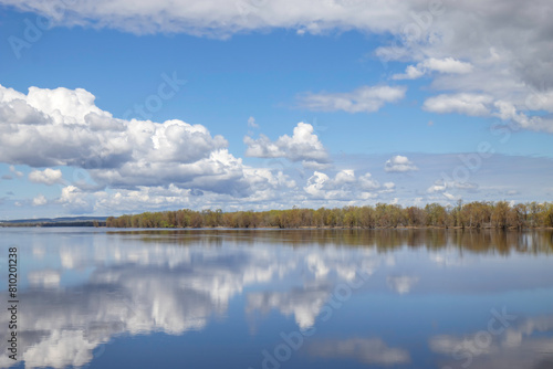 Calm waters with clouds and sky reflected in water, heavy clouds, forested shore in background