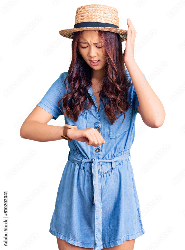 Young beautiful chinese girl wearing summer hat looking at the watch time worried, afraid of getting late Young beautiful chinese girl wearing summer hat looking at the watch time worried, afraid of getting late