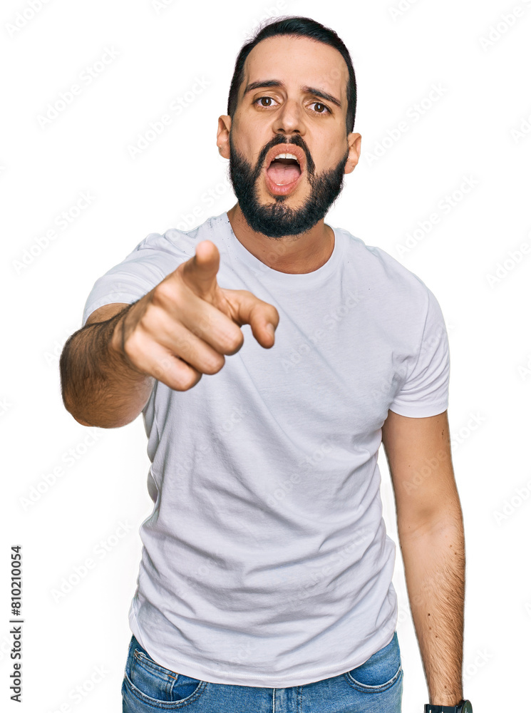 Young man with beard wearing casual white t shirt pointing displeased and frustrated to the camera, angry and furious with you Young man with beard wearing casual white t shirt pointing displeased and frustrated to the camera, angry and furious with you