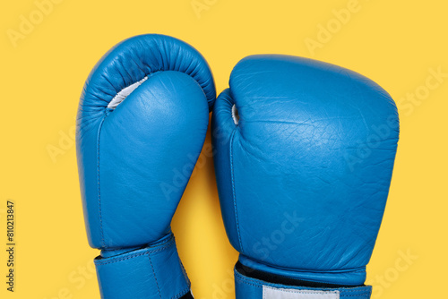 Blue boxing gloves isolated on yellow background. A pair of blue leather boxing gloves close-up top view. Boxing accessories © halcon1