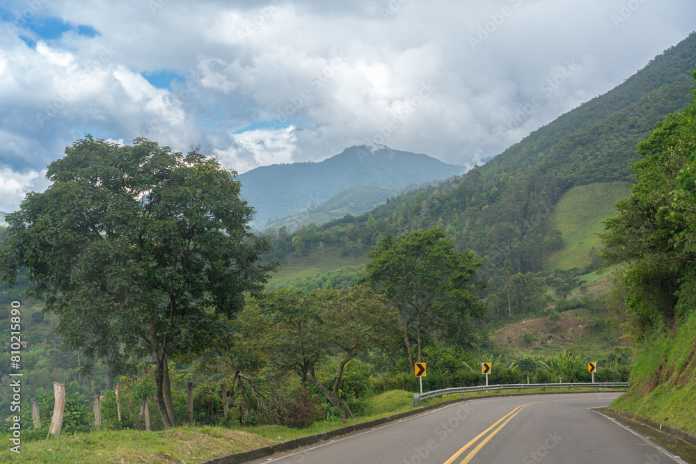Road with double yellow lines with direction traffic signs in a rural Colombian landscape.