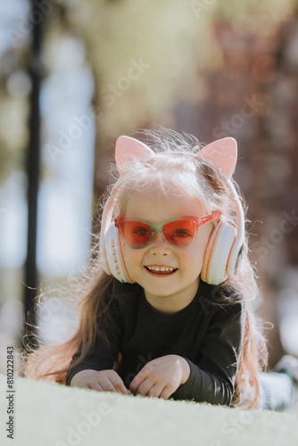 Cute little girl listening to music with headphones on the lawn in summer