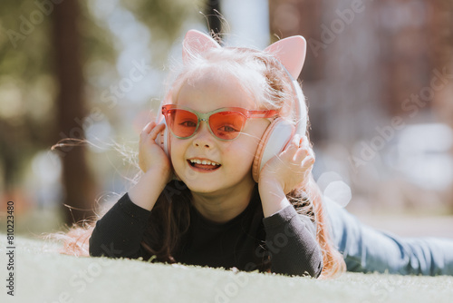 Fototapeta Naklejka Na Ścianę i Meble -  Cute little girl listening to music with headphones on the lawn in summer