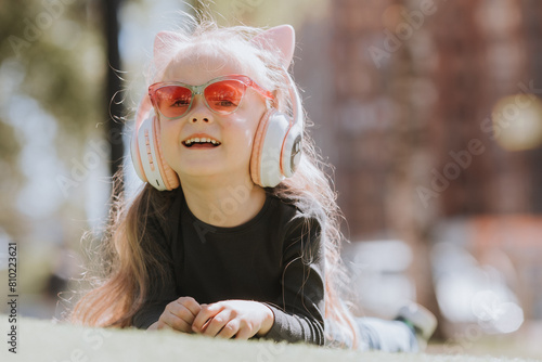 Cute little girl listening to music with headphones on the lawn in summer