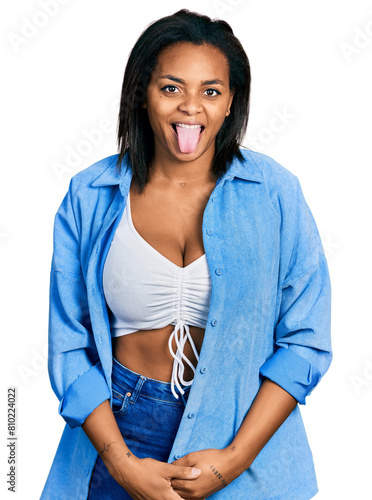 Beautiful hispanic woman wearing casual denim jacket sticking tongue out happy with funny expression. emotion concept.