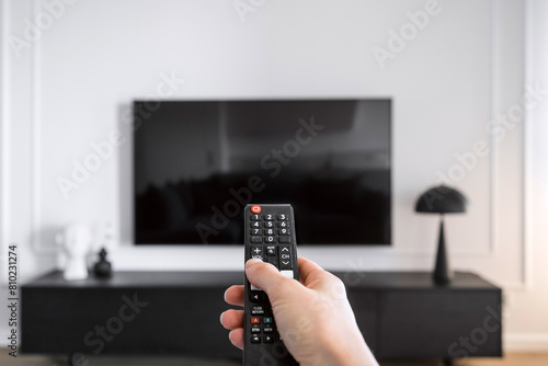 Woman hand hold remote control, press button and turn on television © brizmaker
