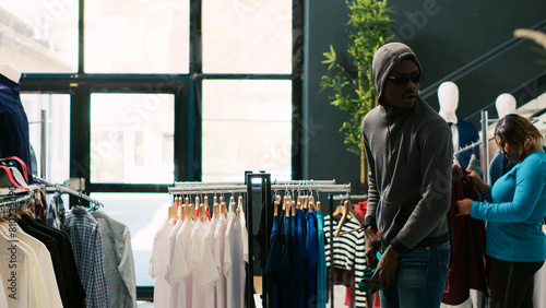 Fotografi African american robber shoplifting clothes, running from modern boutique