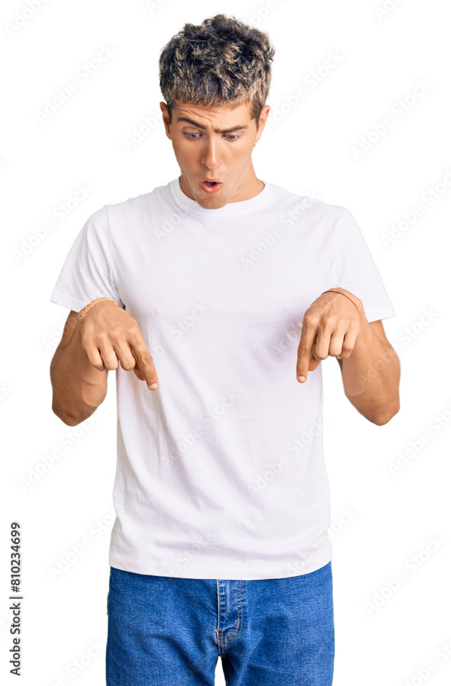 Young handsome man wearing casual white tshirt pointing down with fingers showing advertisement, surprised face and open mouth Young handsome man wearing casual white tshirt pointing down with fingers showing advertisement, surprised face and open mouth