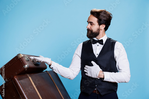 Male bellhop points left and right to create new advertisement, indicating direction sideways while he wears formal attire. Young classy doorman presents ad over blue background. photo