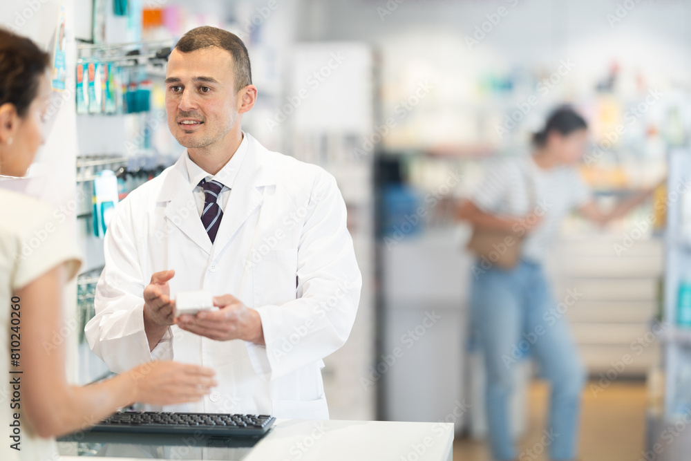 Young male pharmacist giving medicine to adult female buyer at pharmacy