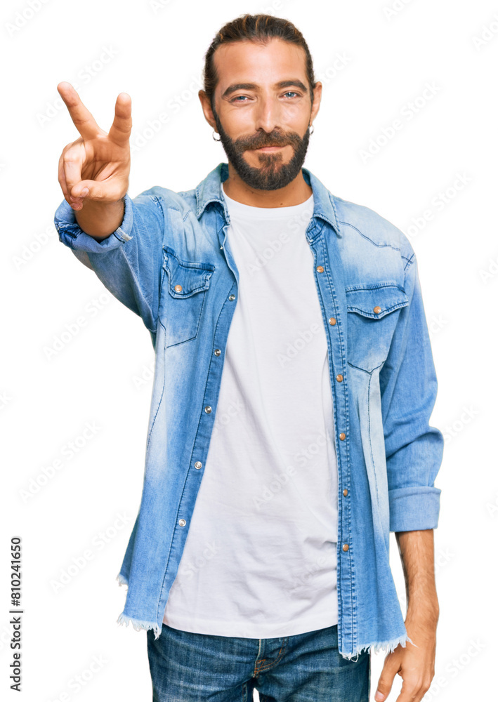 Attractive man with long hair and beard wearing casual denim jacket smiling looking to the camera showing fingers doing victory sign. number two. Attractive man with long hair and beard wearing casual denim jacket smiling looking to the camera showing fingers doing victory sign. number two.