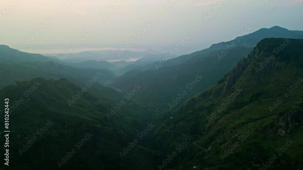 Sunrise peeks over Ella mountains in Sri Lanka, dances across jade-green valleys. Dawn illuminates mist-shrouded peaks, awakening tropical paradise. Travelers witness morning display from aerial view. Sunrise peeks over Ella mountains in Sri Lanka, dances across jade-green valleys. Dawn illuminates mist-shrouded peaks, awakening tropical paradise. Travelers witness morning display from aerial view.