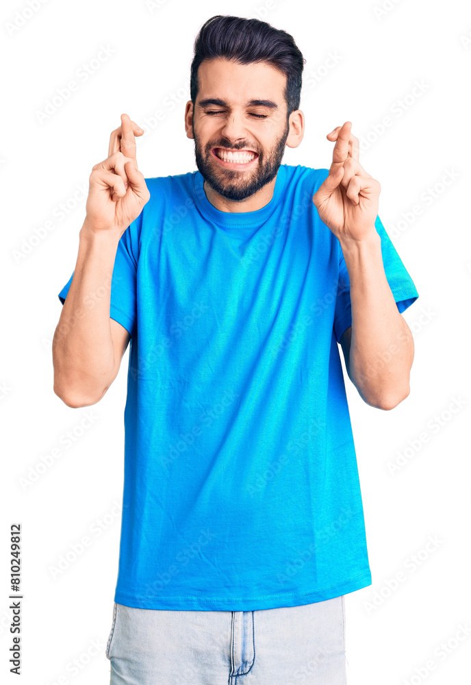 Young handsome man with beard wearing casual t-shirt gesturing finger crossed smiling with hope and eyes closed. luck and superstitious concept. Young handsome man with beard wearing casual t-shirt gesturing finger crossed smiling with hope and eyes closed. luck and superstitious concept.