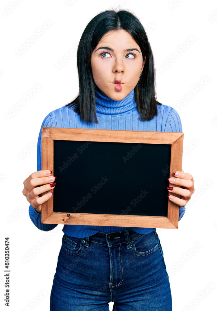 Young brunette woman with blue eyes holding blackboard making fish face with mouth and squinting eyes, crazy and comical. Young brunette woman with blue eyes holding blackboard making fish face with mouth and squinting eyes, crazy and comical.