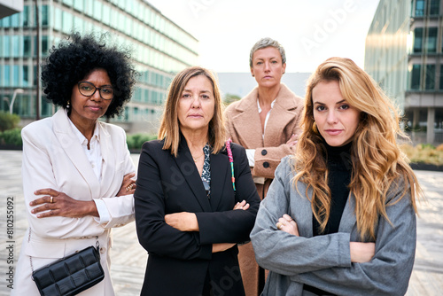 Portrait of multi-ethnic business women of diverse ages posing serious and confident with arms crossed looking empowered at camera outside office building. Earnest female only work team photo