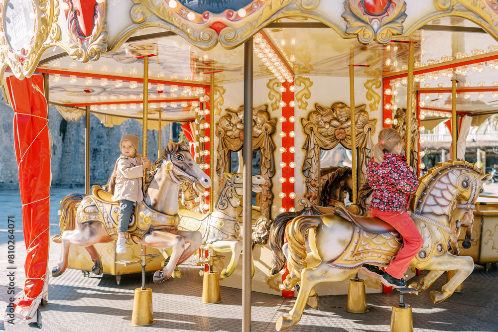 Little children ride colorful toy horses on a carousel while holding onto a pole