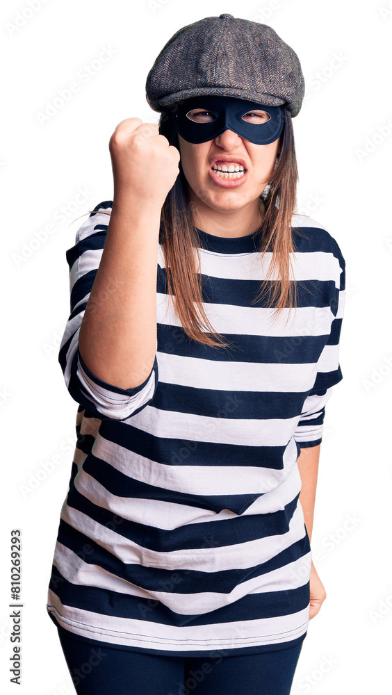 Young beautiful brunette woman wearing burglar mask angry and mad raising fist frustrated and furious while shouting with anger. rage and aggressive concept. Young beautiful brunette woman wearing burglar mask angry and mad raising fist frustrated and furious while shouting with anger. rage and aggressive concept.