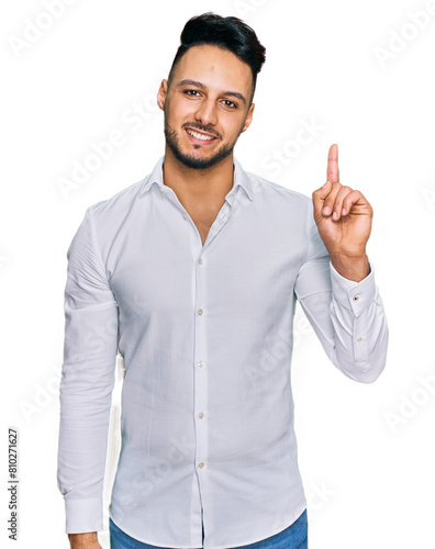 Young arab man wearing casual clothes showing and pointing up with finger number one while smiling confident and happy.