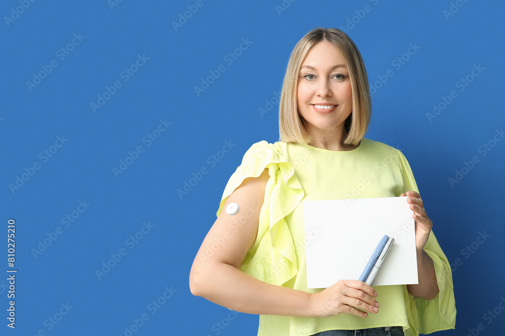 Obraz premium Woman with glucose sensor for measuring blood sugar level, lancet pens and blank paper on blue background. Diabetes concept