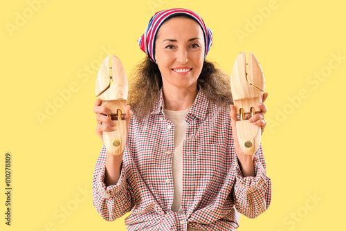 Female shoemaker with wooden shoe trees on yellow background