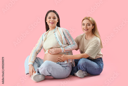 Mature doula with pregnant woman sitting on pink background