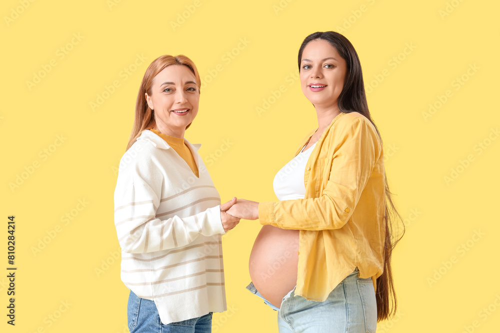 Mature doula with pregnant woman holding hands on yellow background Mature doula with pregnant woman holding hands on yellow background