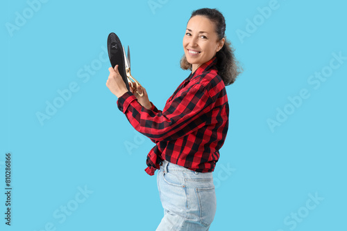 Happy female shoemaker cutting insole on blue background