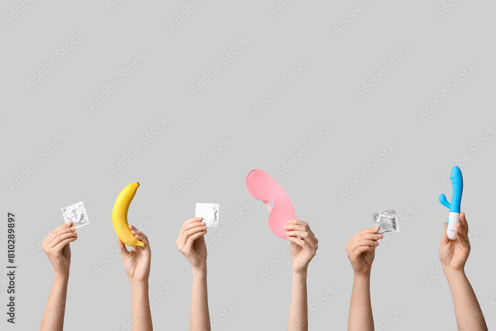 Female hands with condoms, sex toys and banana on grey background Female hands with condoms, sex toys and banana on grey background