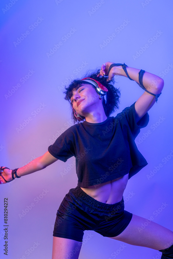 A woman is dancing and wearing headphones. She is smiling and she is enjoying herself. young woman listening to music on colorful background A woman is dancing and wearing headphones. She is smiling and she is enjoying herself. young woman listening to music on colorful background