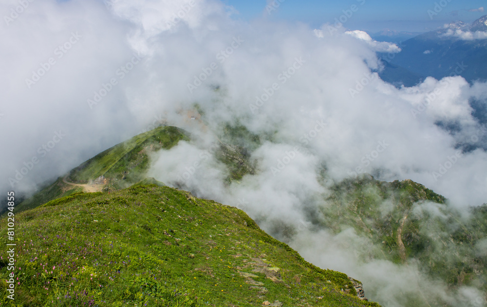 The tops of the green hills on Krasnaya Polyana in Sochi in a big white cloud and a space for copying. Concept - the beauty of nature and mountain trekking The tops of the green hills on Krasnaya Polyana in Sochi in a big white cloud and a space for copying. Concept - the beauty of nature and mountain trekking