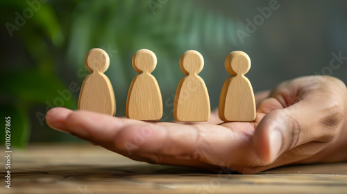 Human resources and hiring, A hand holds wooden human figures against a blurred green background