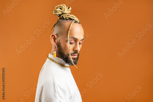 Confident black gay man with bright makeup standing isolated on orange background, dressed white. Exudes sense of pride and individuality. Diversity power of personal style