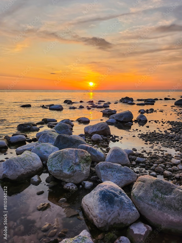 The setting sun casts a golden glow on the rocky beach. The waves are splashing gently against the rocks. The sky is ablaze with color, and the scene is one of peace and tranquility. The setting sun casts a golden glow on the rocky beach. The waves are splashing gently against the rocks. The sky is ablaze with color, and the scene is one of peace and tranquility.