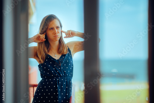 Woman Standing in the Balcony Covering her Ears. Unhappy woman hearing loud music coming from an outdoors music festival
