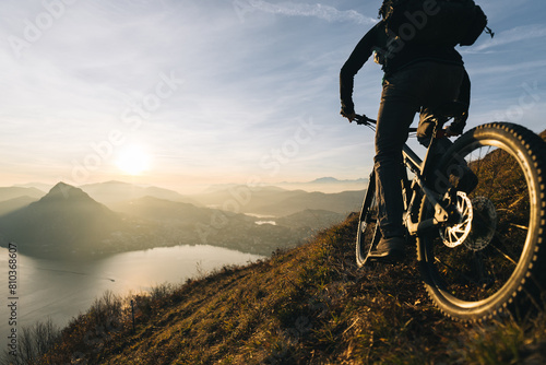 Silhouette of a cyclist enjoying a sunrise ride on a mountain trail with a scenic lake view © Bryan