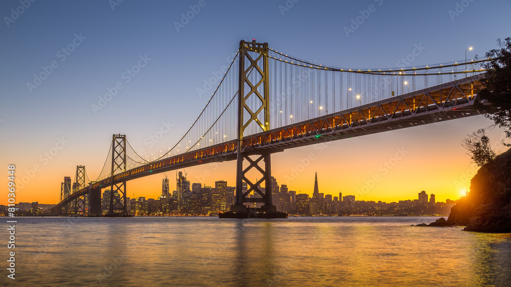 Golden sunset behind city skyline with suspension bridge