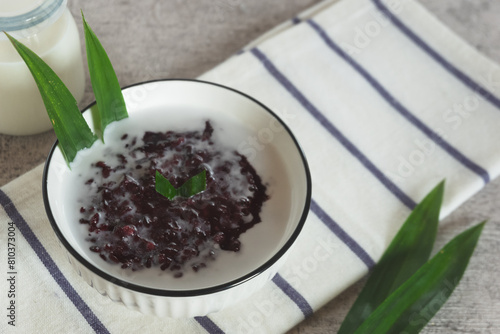 Black sticky rice porridge, a typical Indonesian dessert. Black sticky rice porridge with coconut milk, sugar and pandan leaves. Served in a white bowl. photo