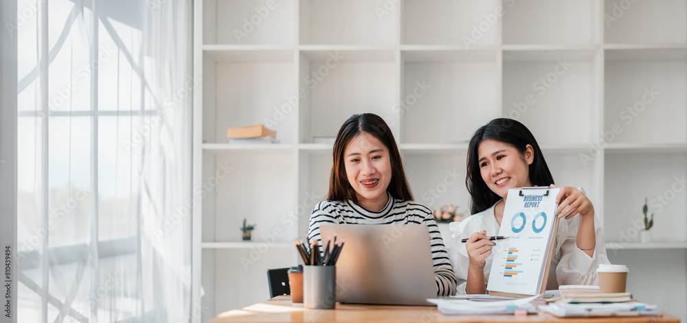 Professional team works together analyzing a business report, with a laptop and documents on their desk in an office setting. Professional team works together analyzing a business report, with a laptop and documents on their desk in an office setting.