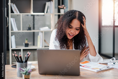 Ecstatic businesswoman receives good news on her laptop, reacting with joy amidst her busy workspace.