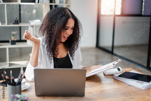 Surprised businesswoman reacts to a financial document while working at her desk with a laptop and calculator.