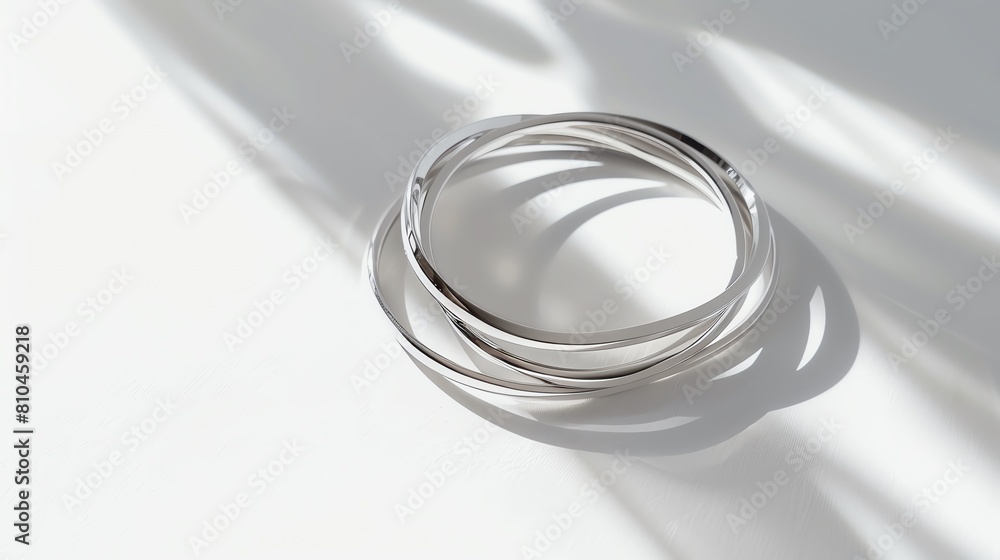 A set of minimalist silver bangles on a stark white background, highlighted by soft shadows A set of minimalist silver bangles on a stark white background, highlighted by soft shadows