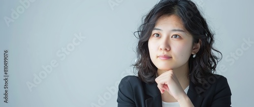 A Japanese woman in her thirties, with a thoughtful expression and her hand on her chin, wearing a casual suit against a white background banner for advertising. copy space for text.