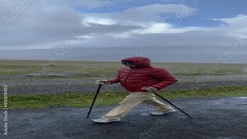 Adult woman walking in the rain wearing a waterproof jacket and pants, using trekking poles. 4K video with camera movement