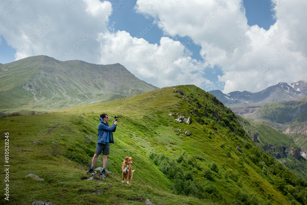 An explorer captures the essence of the mountains, accompanied by a loyal Nova Scotia Duck Tolling Retriever dog An explorer captures the essence of the mountains, accompanied by a loyal Nova Scotia Duck Tolling Retriever dog