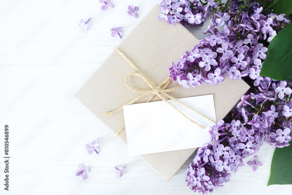 Gift box with blank card and lilac flowers on white wooden background, copy space. Top view, flat lay Gift box with blank card and lilac flowers on white wooden background, copy space. Top view, flat lay