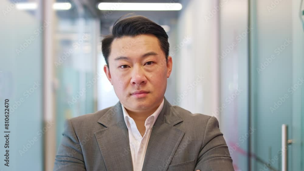 Close up portrait of chinese gentleman standing with crossed arms within contemporary corporate office. Serious young male dressed impeccably in formal attire gazing at camera with determination. Close up portrait of chinese gentleman standing with crossed arms within contemporary corporate office. Serious young male dressed impeccably in formal attire gazing at camera with determination.