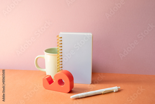 Obraz na płótnie Workspace office desk with notebook, mug cup, pen, tape dispenser. pink orange background w salonie